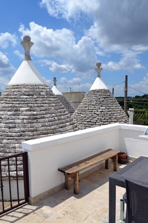 A rooftop terrace with stone conical structures, a wooden bench, and a metal table. - Coppola di Seta (Locorotondo)