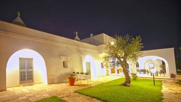 Un patio con un edificio blanco, arcos, un banco y un árbol.