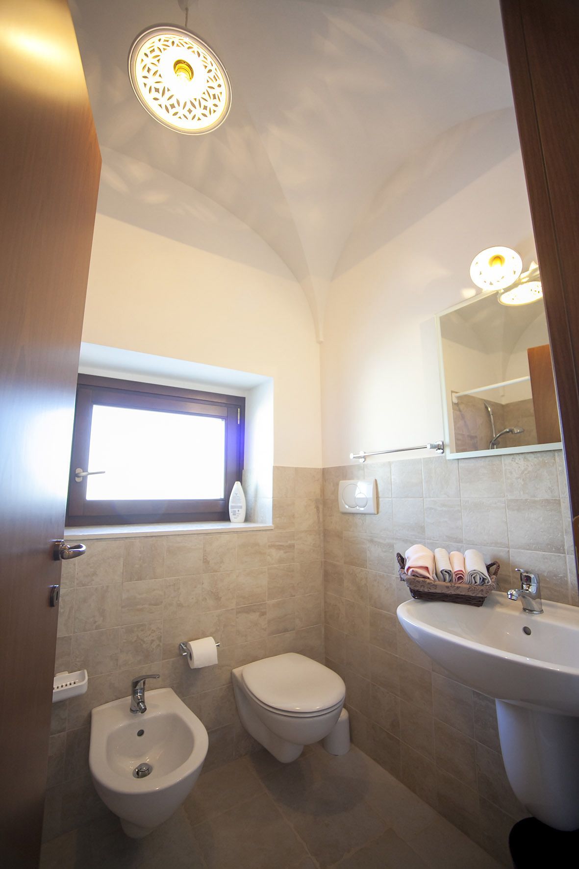 A bathroom with a bidet, toilet, sink, and a window with a towel rack.