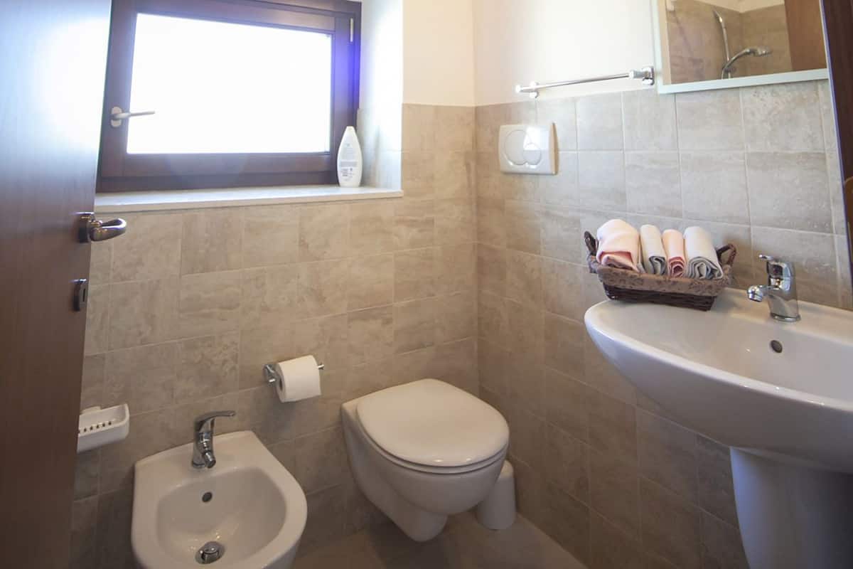 A bathroom with a bidet, toilet, sink, and a window with a towel rack.