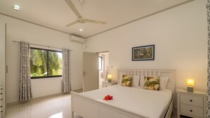 Une chambre à coucher avec un lit, un ventilateur de plafond, une table de chevet avec une lampe et une fenêtre avec des rideaux.