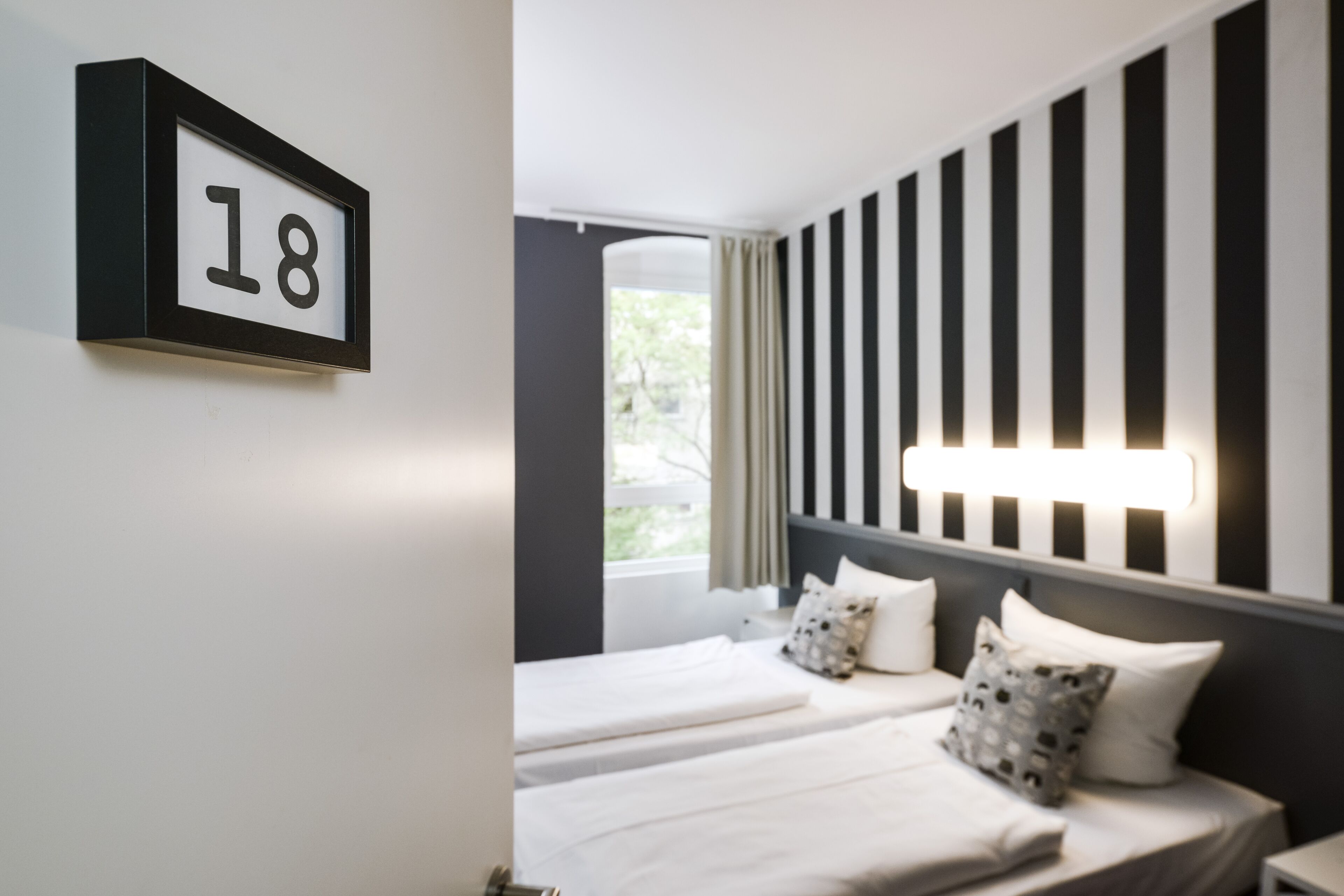 Una camera d'albergo con due letti, una parete a righe bianche e nere e un cartello con il numero 18.