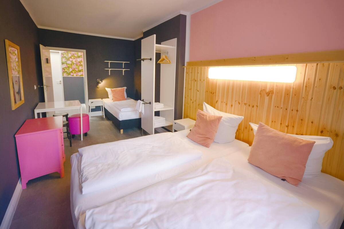 A hotel room with a large bed, a desk, a chair, and a wardrobe.