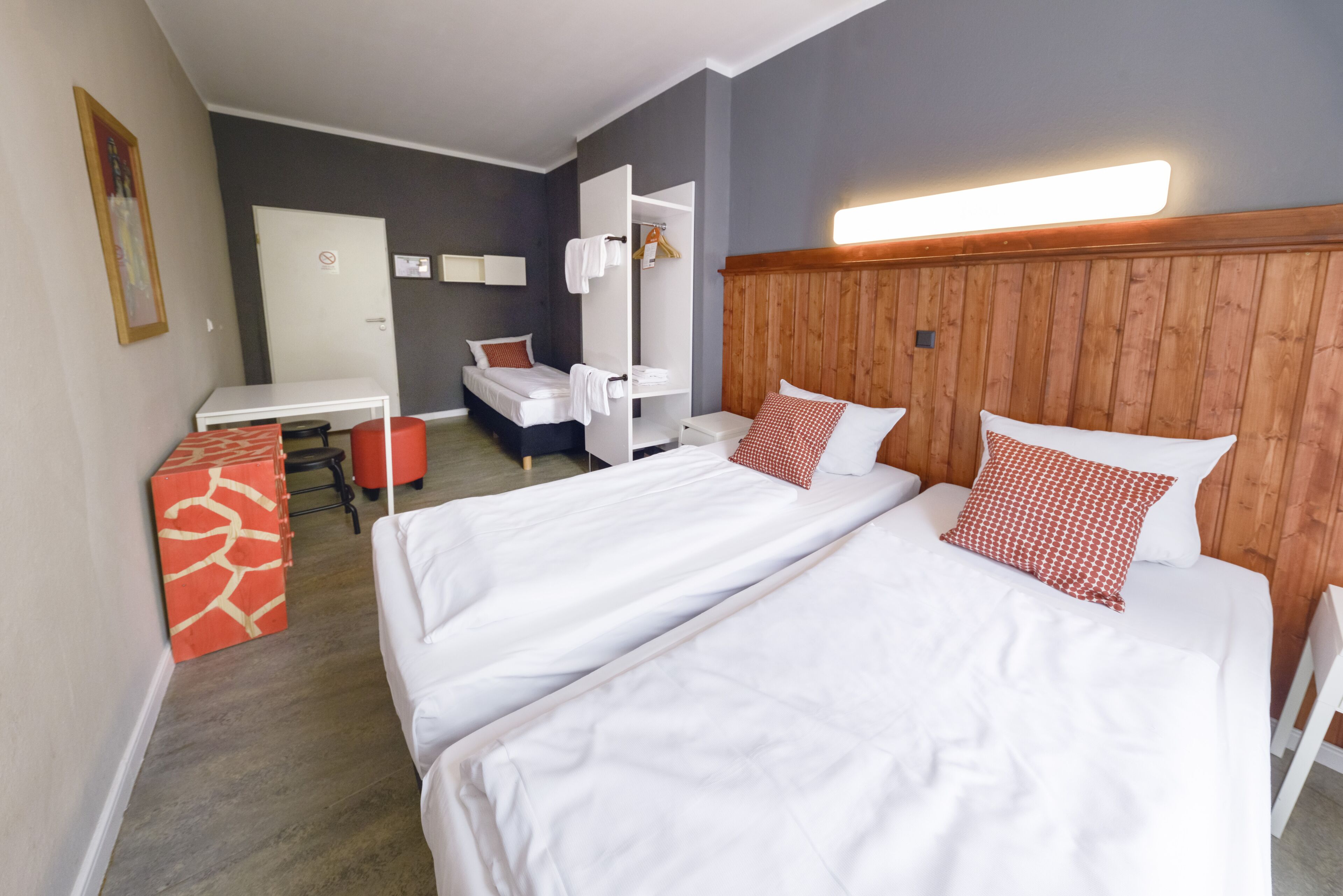 A hotel room with two beds, a desk, a chair, and a wardrobe.