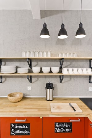 Een keuken met houten planken waarop witte serviesdelen, een houten kom, een waterkoker en een snijplank staan.