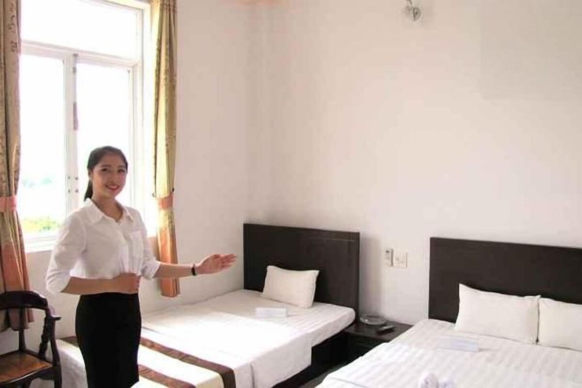 Una habitación de hotel con dos camas individuales, una mesita de noche de madera y una ventana con cortinas.