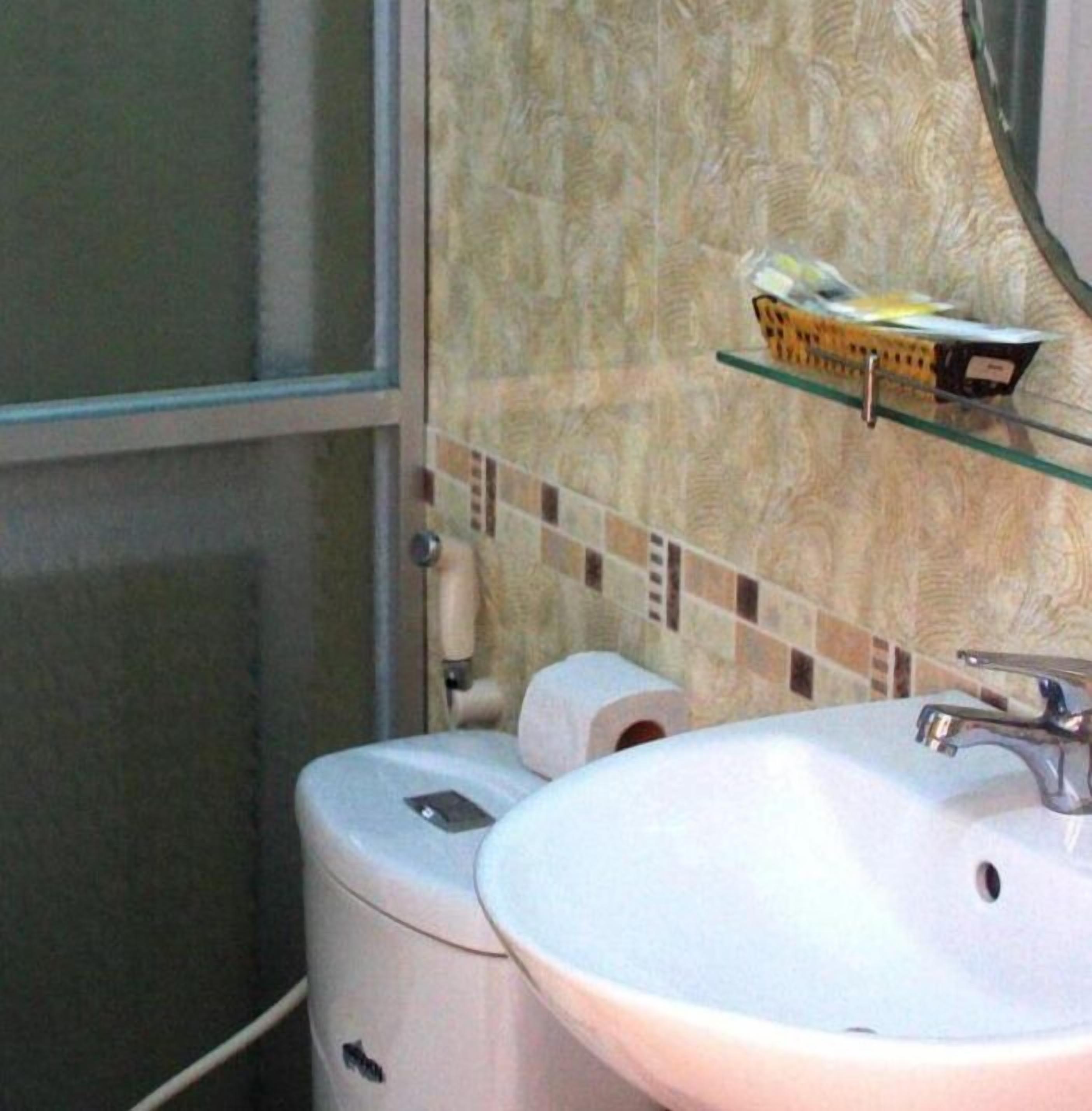 A bathroom with a white sink, toilet, and a glass shelf above the toilet holding toiletries.