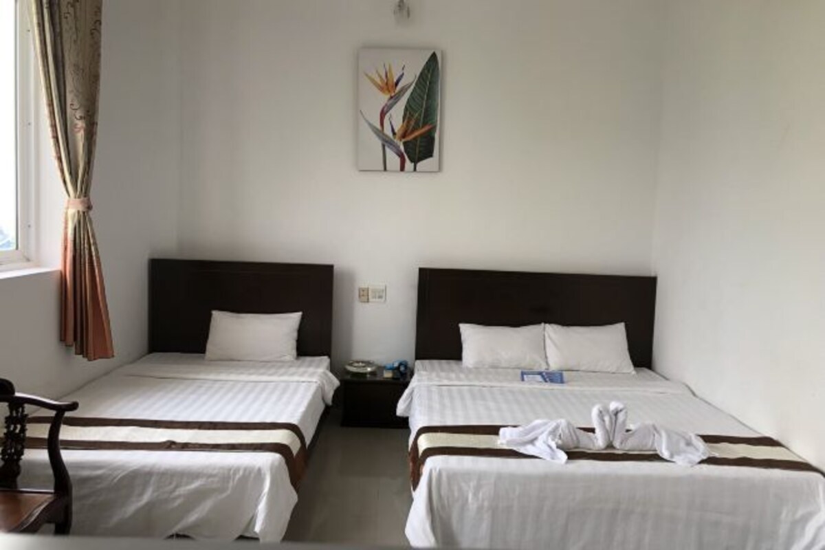 Habitación de hotel con dos camas individuales, una mesita de noche, una silla y una ventana con cortinas.