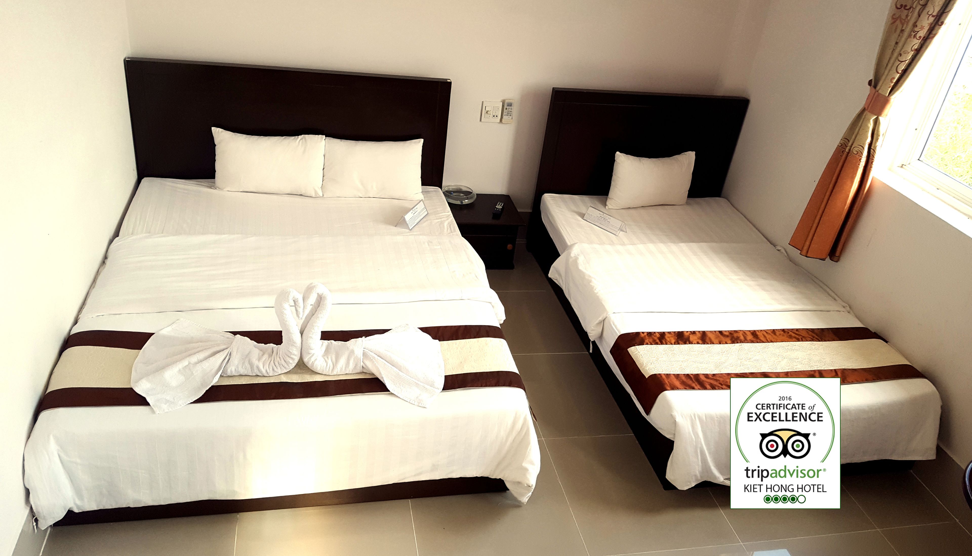 Two twin beds with white linens, a nightstand with a lamp, and a window with curtains.