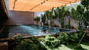 Una piscina con un toldo de madera, rodeada de exuberante vegetación tropical.