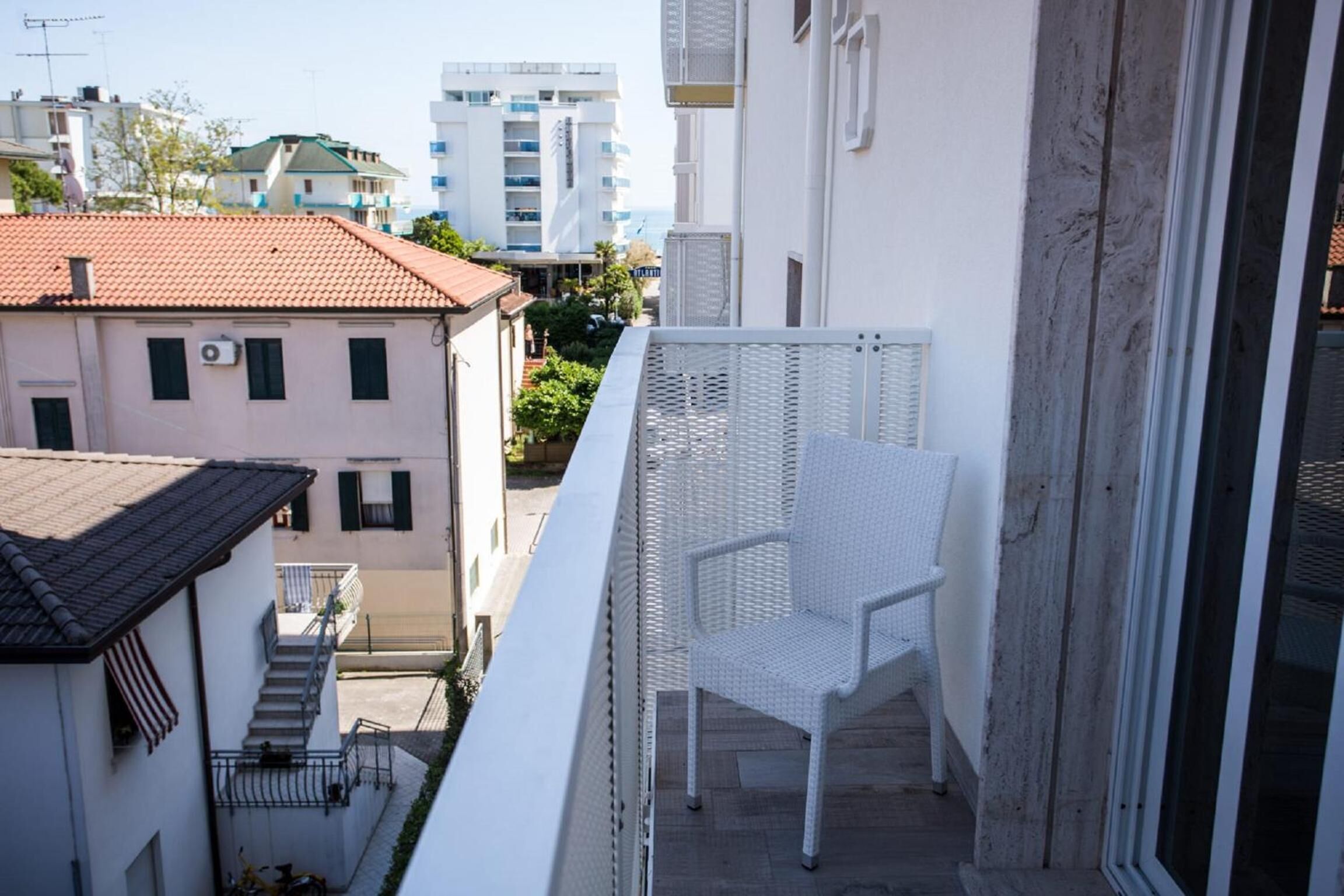 A balcony with a white wicker chair, a white railing, and a view of neighboring buildings.