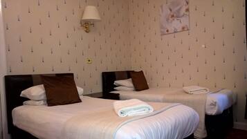 A hotel room with two beds, each with a pillow and a folded towel. There is a wall-mounted lamp and a framed picture on the wall.