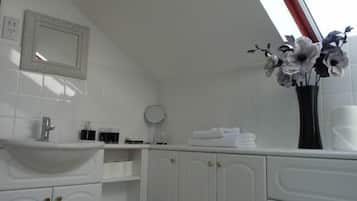 A bathroom with a white sink, mirror, and cabinets. There is a vase with flowers on the counter.