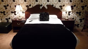 Habitación de hotel con cama, dos lámparas de noche, cabecero de madera, manta negra decorativa, almohada negra y mesita de noche con un cajón.