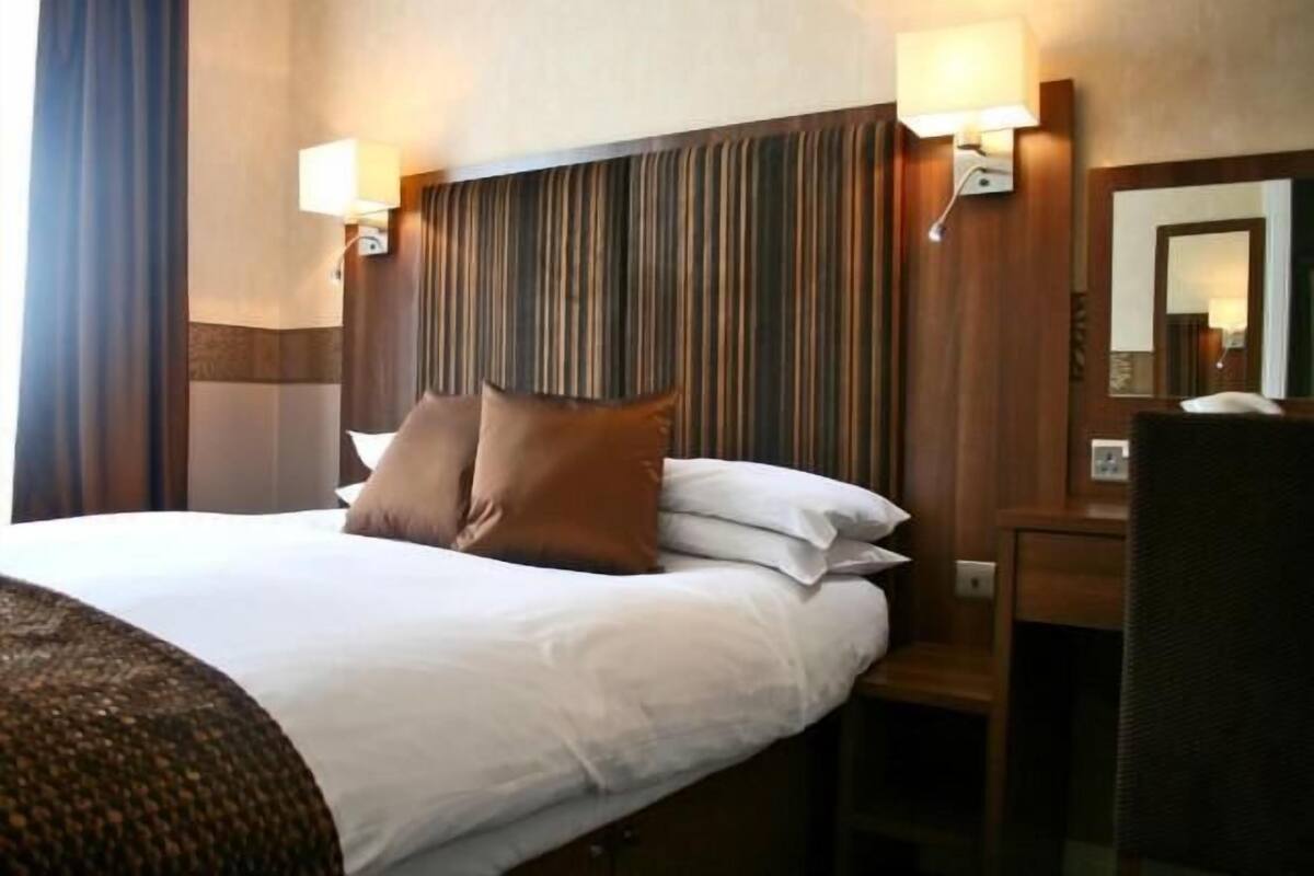 A hotel room with a large bed, two wall-mounted lamps, a wooden headboard, and a mirror.