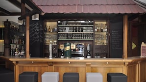 A bar area with a wooden counter, multiple stools, and shelves stocked with bottles and glasses. - Rennsteighotel Herrnberger Hof (Neuhaus am Rennweg)