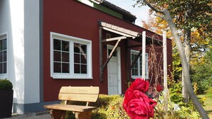 A red building with a white door, a bench, and a red rose in the foreground. - Rennsteighotel Herrnberger Hof (Neuhaus am Rennweg)