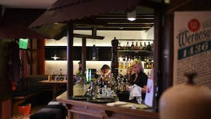 A bar area with a wooden counter, shelves with bottles, and a sign for 'Wernesg 1430'. - Rennsteighotel Herrnberger Hof (Neuhaus am Rennweg)