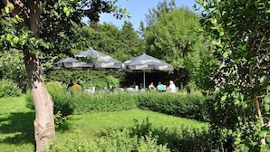 An outdoor seating area with tables and umbrellas, surrounded by greenery and trees. - Rennsteighotel Herrnberger Hof (Neuhaus am Rennweg)