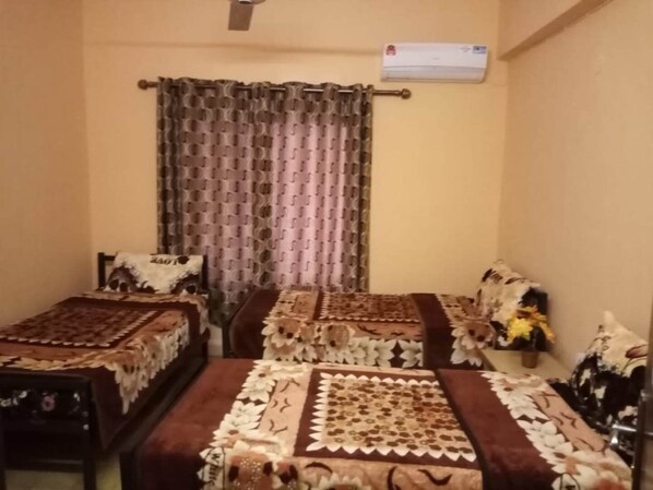 A room with two beds, each covered with patterned bedspreads. There is a ceiling fan and an air conditioning unit on the wall.
