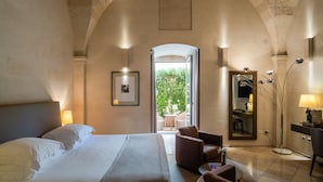 Camera d'albergo con un letto grande, una zona salotto con una poltrona, una scrivania con una lampada, uno specchio e vista sull'esterno.