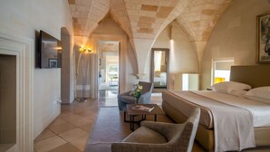 Una camera d'albergo con soffitto a volta alto, un letto, una poltrona, un tavolino e uno specchio.