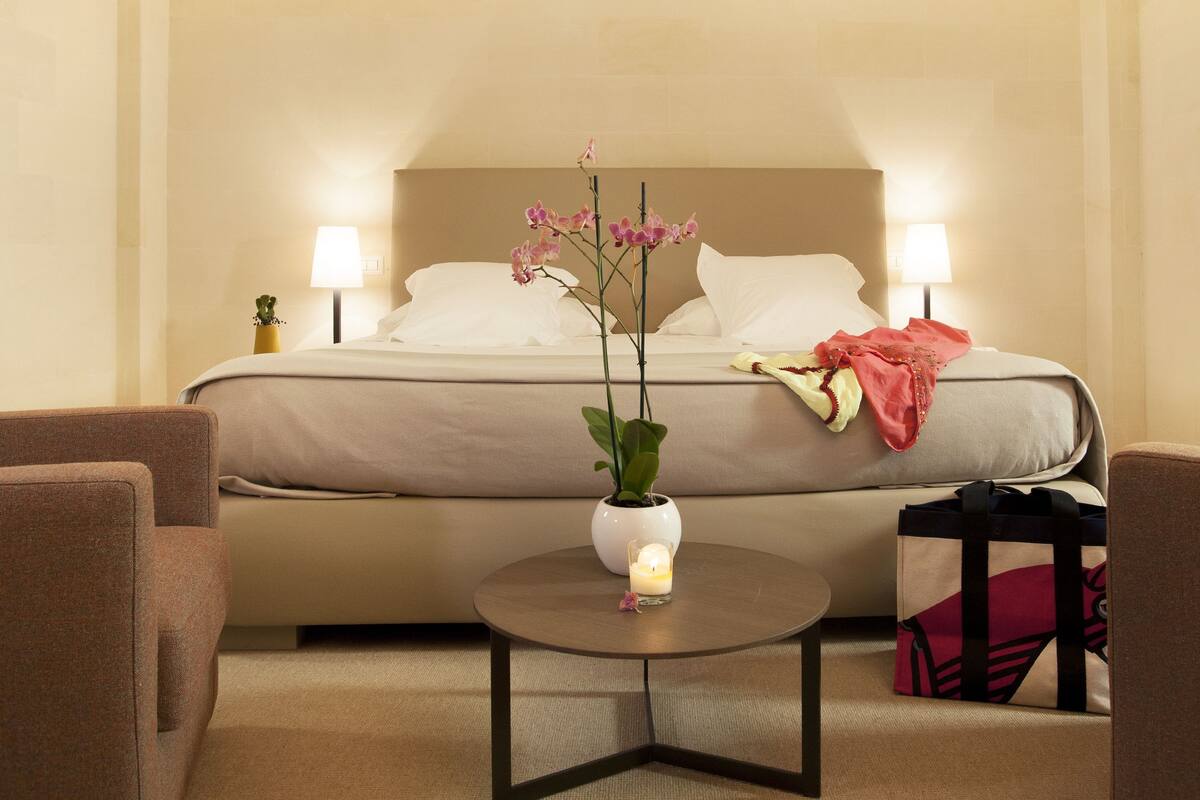 Ett hotellrum med en säng, två sänglampor, ett litet bord med ett ljus, en krukväxt och två fåtöljer.