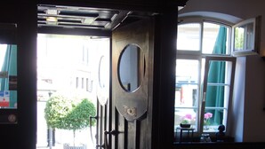 Interieur van een hotelkamer met een groot raam, een deur met een spiegel en een kleine tafel met een kom en een glas.