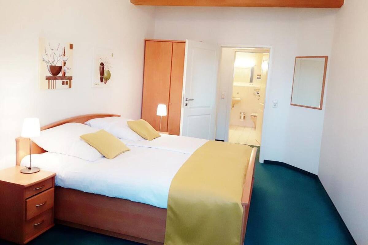 Ein Schlafzimmer mit Bett, Nachttischen, einem Kleiderschrank und einem durchgehenden Türbogen sichtbaren Badezimmer.