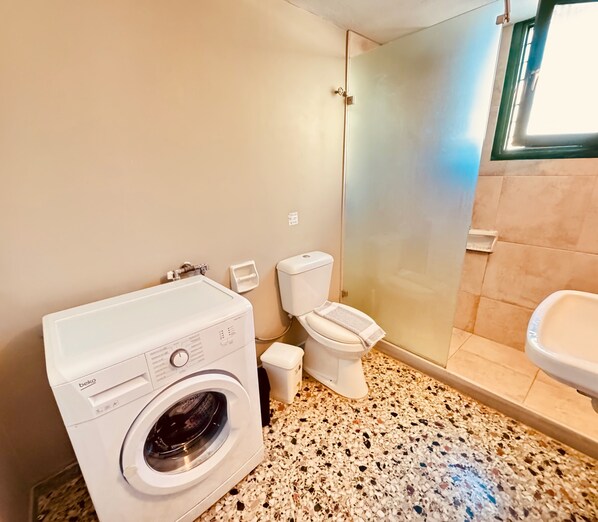 A compact bathroom with a washing machine, toilet, and sink. - Domenica Apartments (Rethymno)