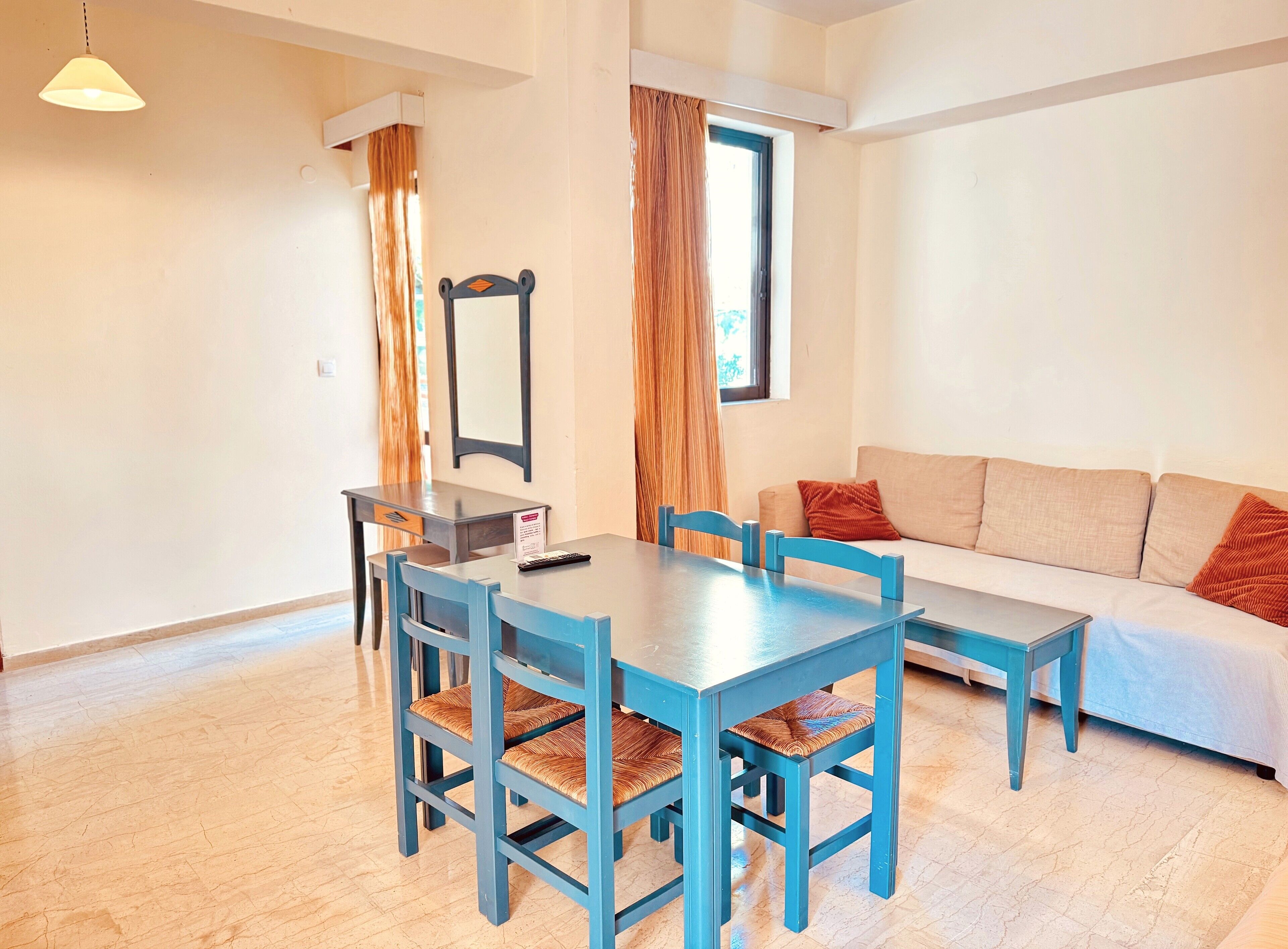 Een eetgedeelte met een tafel en stoelen, een bank, een spiegel en een raam met gordijnen.