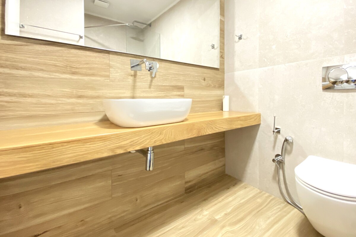 A modern bathroom with a wooden vanity, a white sink, and a toilet.