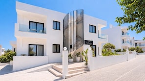 A modern building with a white facade, balconies, and a staircase leading to the entrance. - Domenica Apartments (Rethymno)