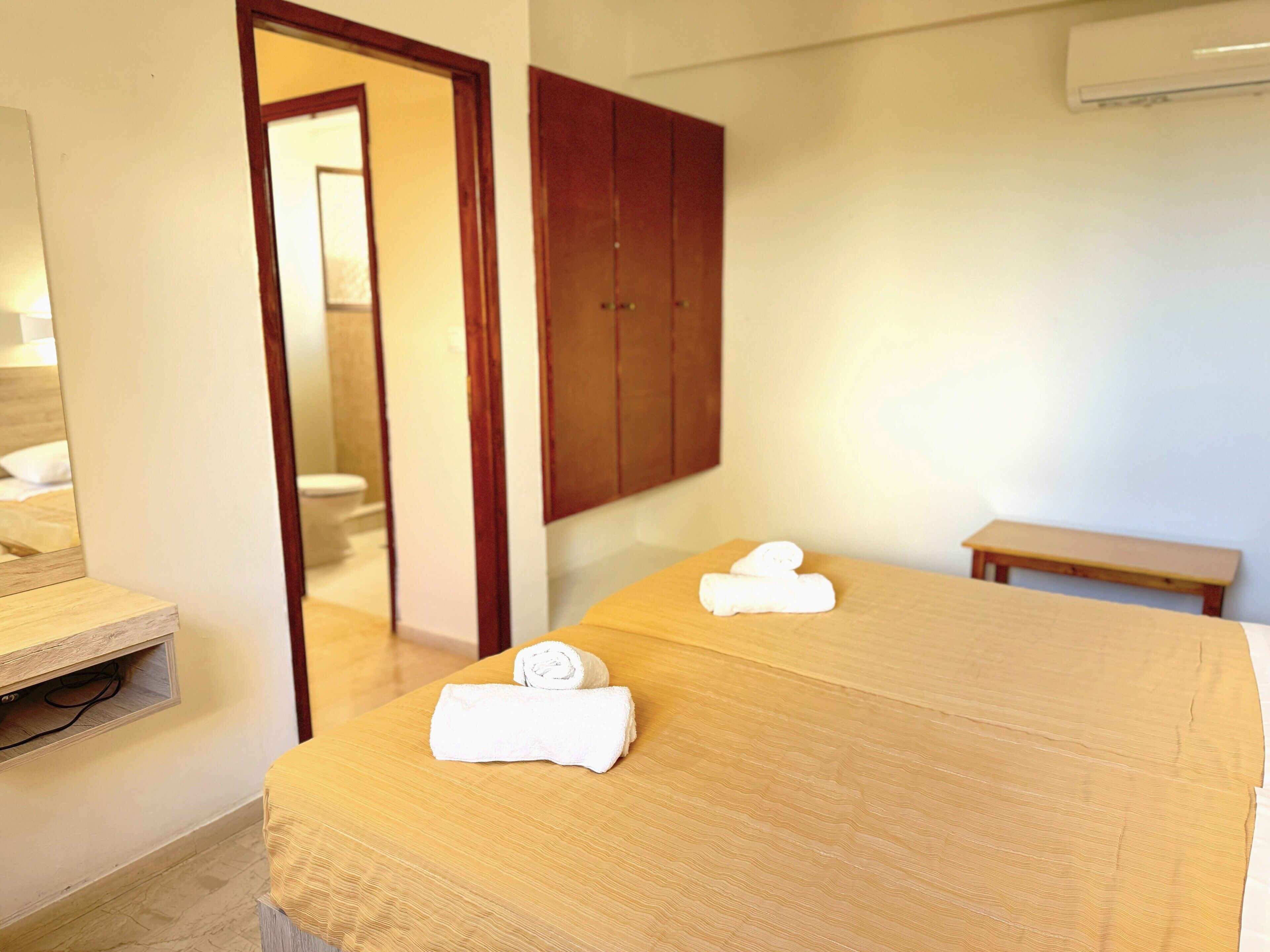 Une chambre d’hôtel avec un lit, un banc en bois, un miroir et une armoire.