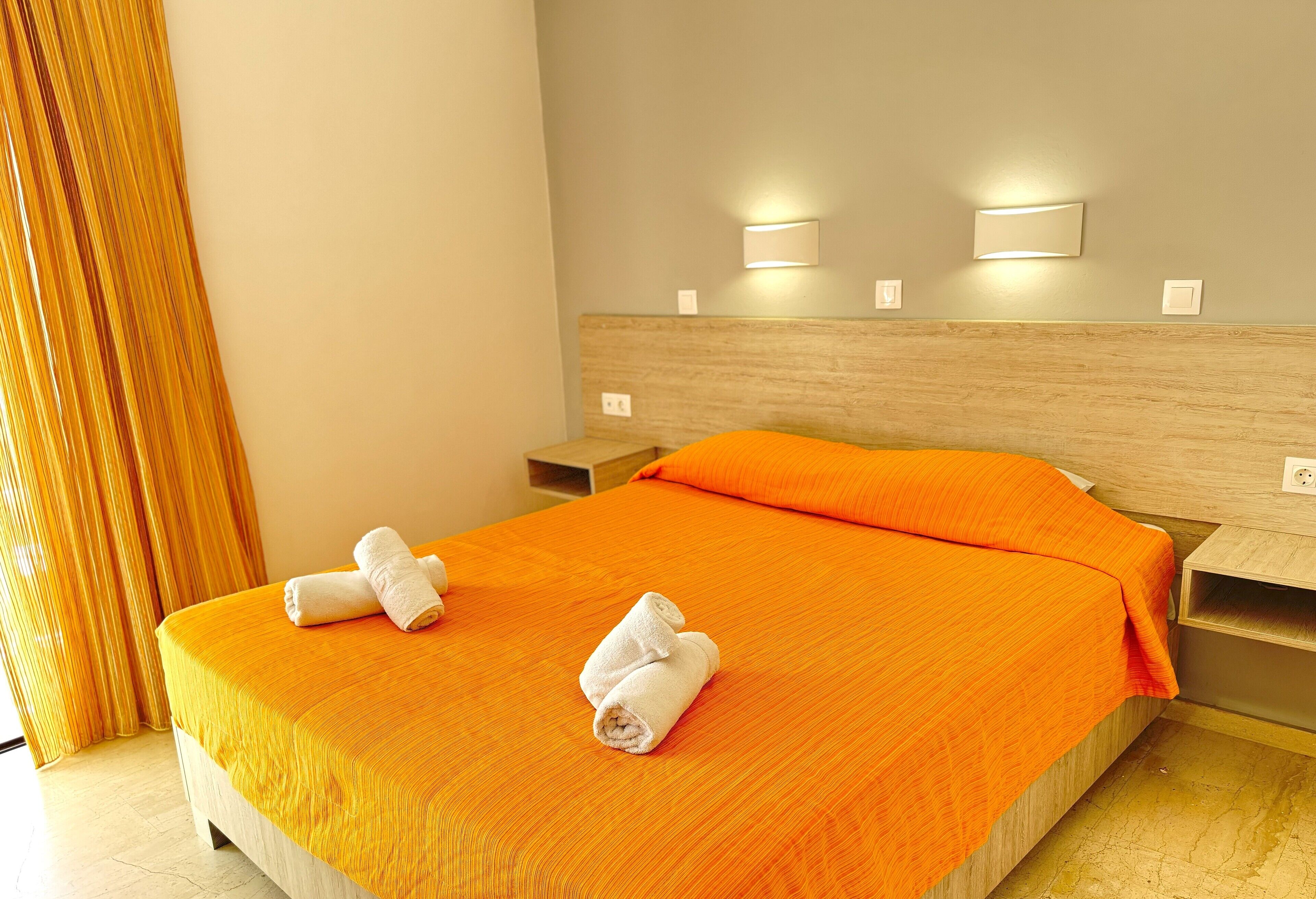 A hotel room with a bed, two wall-mounted light fixtures, and a wooden headboard.