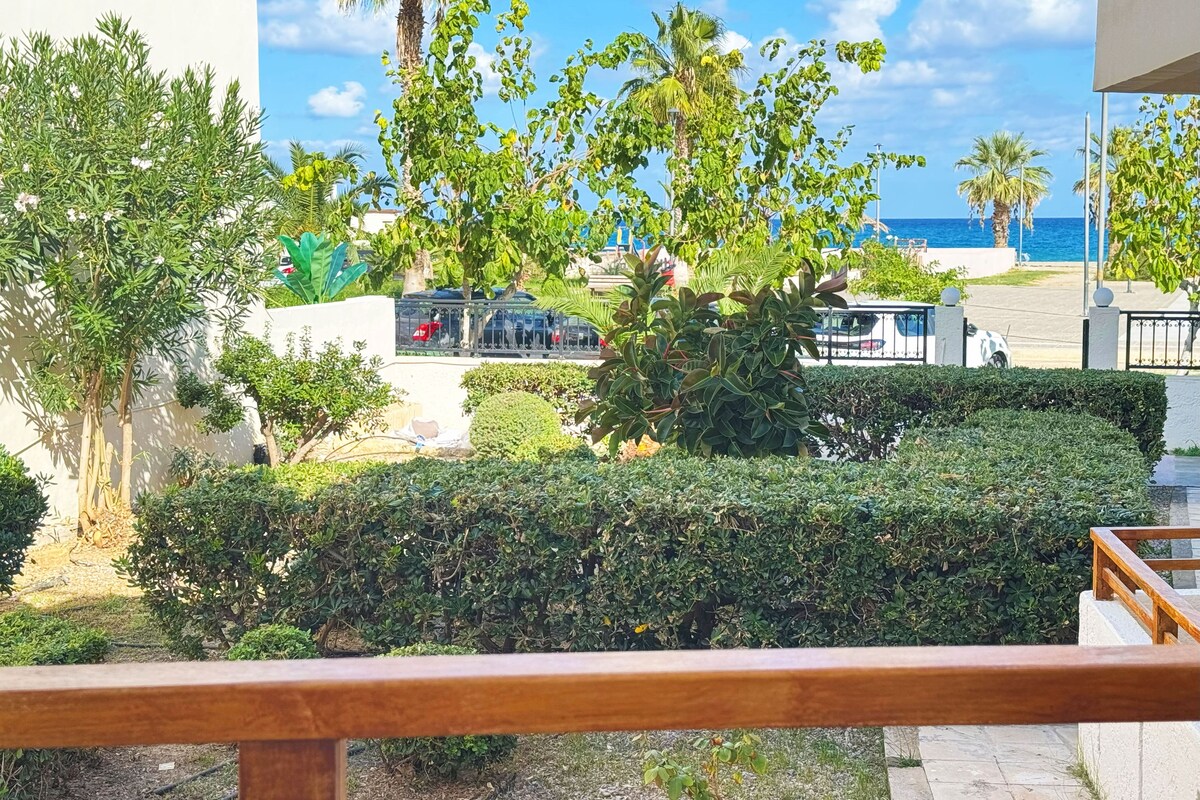 A view of a landscaped area with palm trees and a beach in the background.