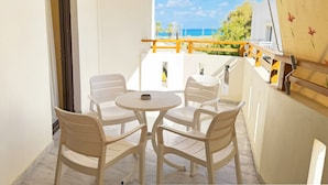Un balcón con una mesa y cuatro sillas, baranda de madera y vista al mar.