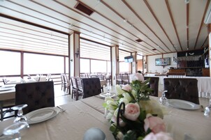 A dining area with tables set for service, large windows, and a television mounted on the wall.