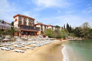 Un hotel frente al mar con varios pisos, una playa con tumbonas y sombrillas, y vista al océano.