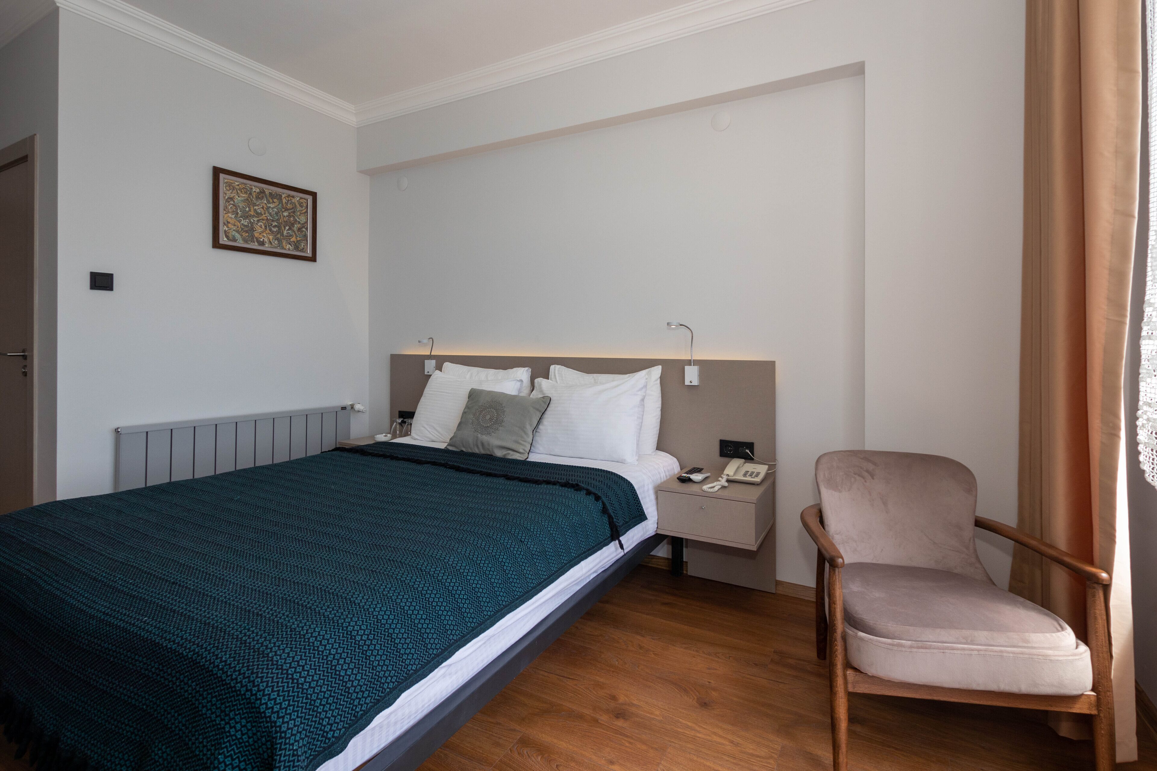Un dormitorio ordenado con cama, mesita de noche, silla e imagen enmarcada en la pared.