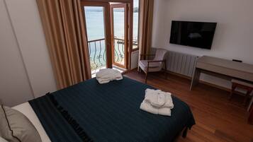 Habitación de hotel con cama, escritorio, silla, televisor y vista al mar a través de un ventanal.