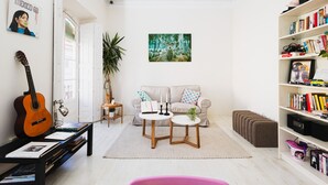 A living room with a guitar, bookshelves, a sofa, and a coffee table. - Hostal Vidamia (Málaga)