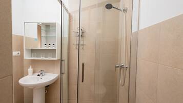 Un baño con ducha de vidrio, lavamanos sobre pedestal y mueble de espejo.