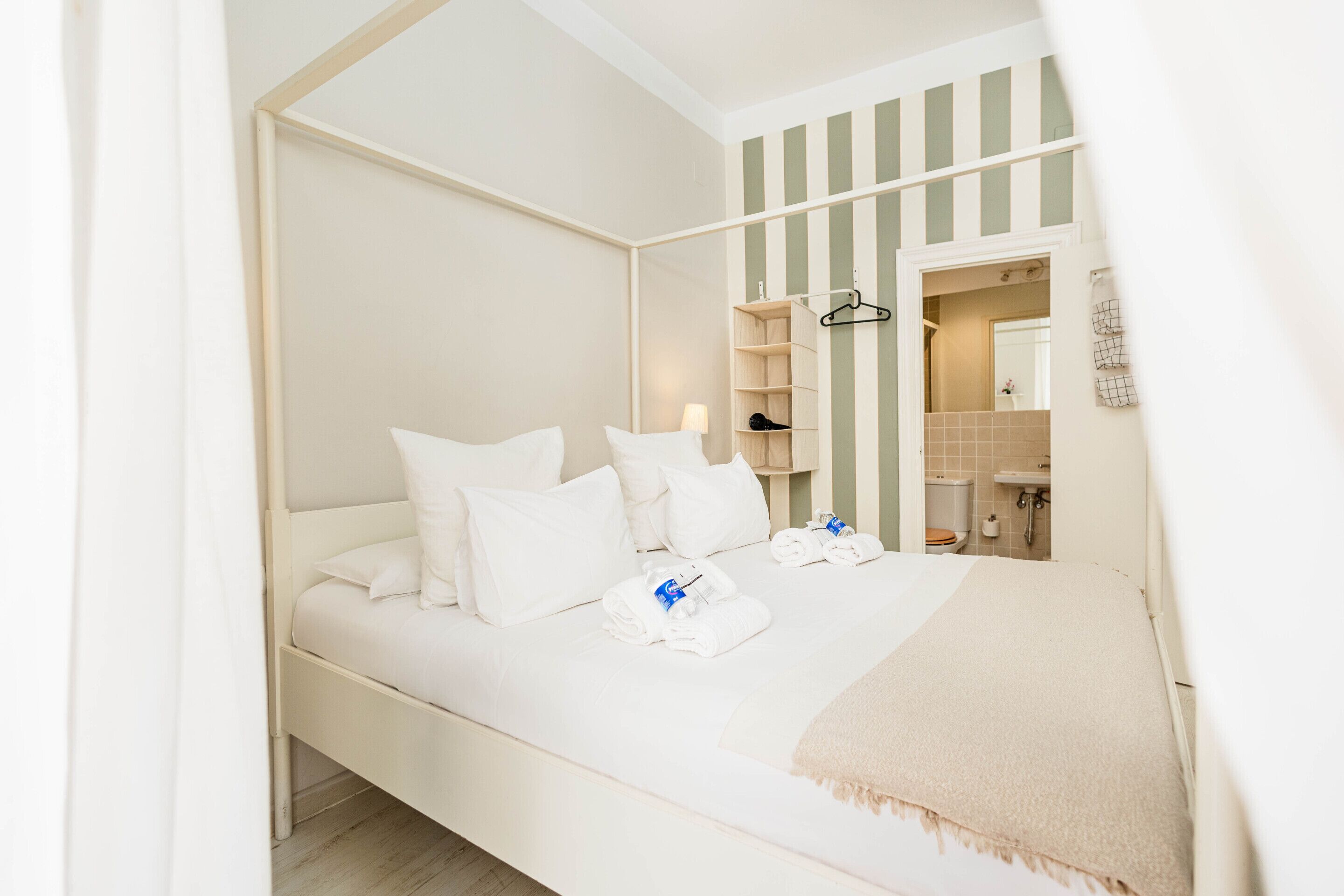 A single bed with white bedding, a bedside table, and a hanging coat rack.