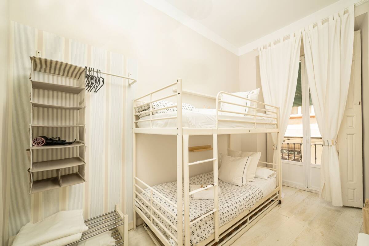Habitación con literas, un perchero y una puerta con cortinas.