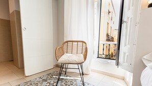 A room with a wicker chair, patterned floor, and a view of a building through a door. - Hostal Vidamia (Málaga)