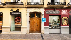 A building with a wooden door labeled "VIDAMIA," a sign for "EMPANADAS ARGENTINAS," and a blue sign with a white 'H' indicating a hotel. - Hostal Vidamia (Málaga)