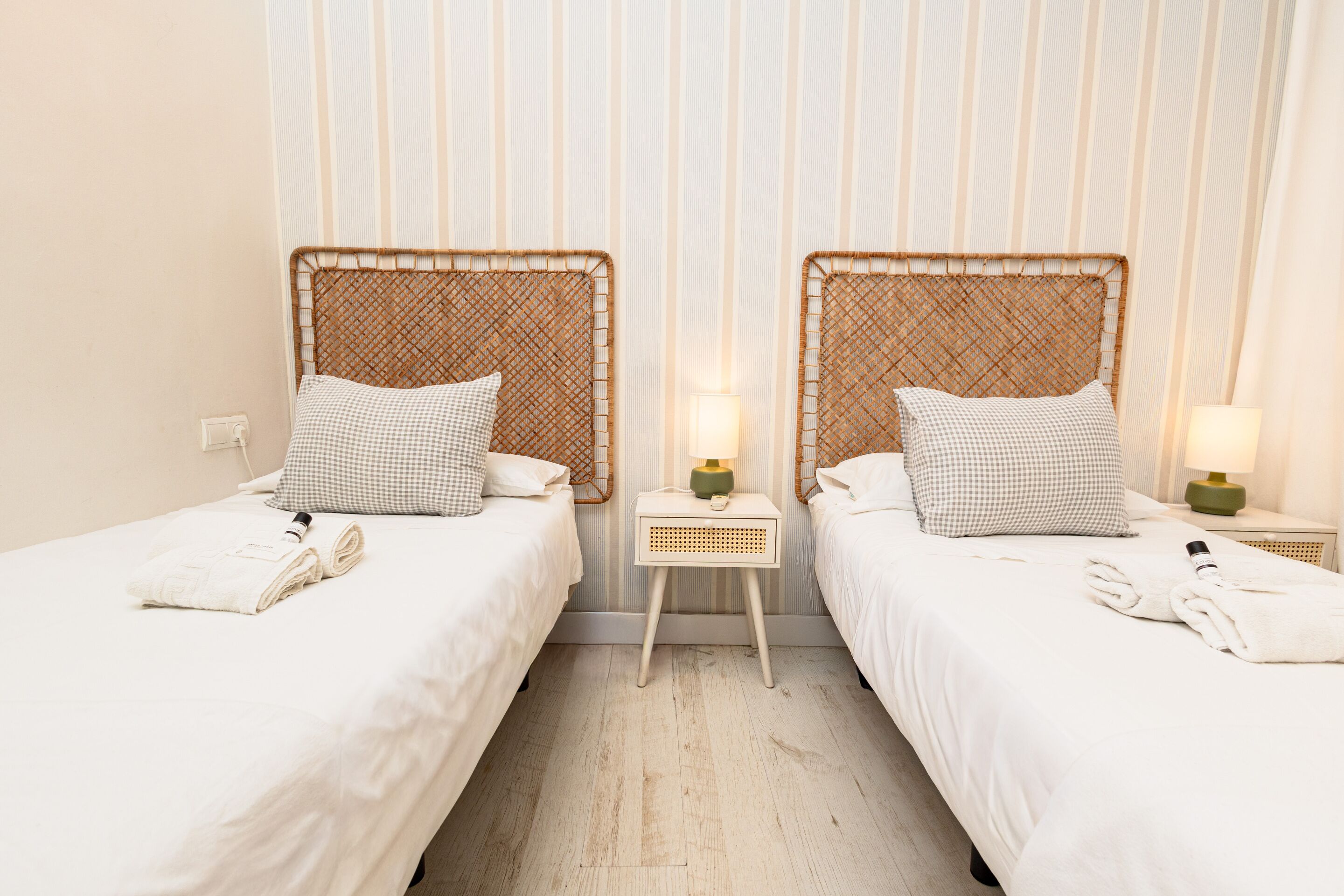 A hotel room with two single beds, each with a wicker headboard, white linens, and a small bedside table with a lamp.