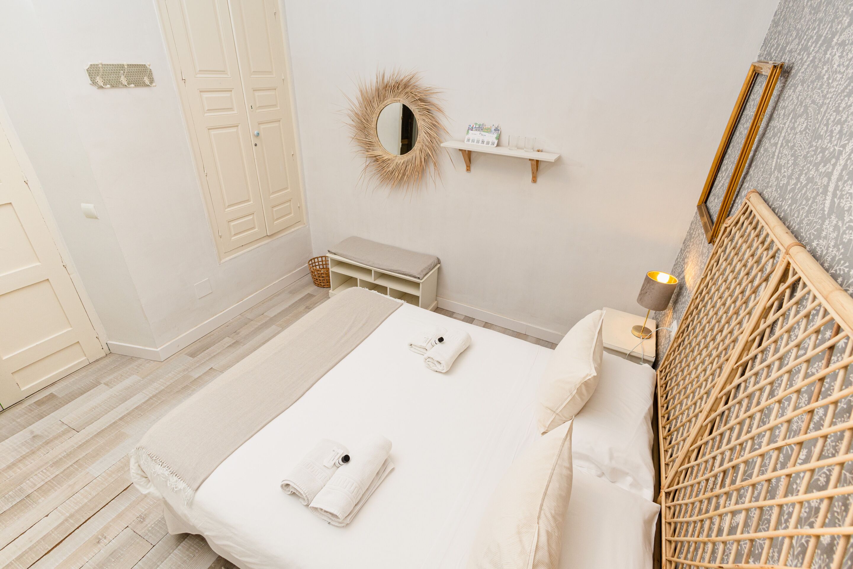 Un dormitorio ordenado con cama, mesitas de noche, un espejo y una repisa con artículos de aseo.