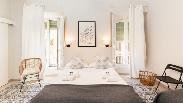 A hotel room with a bed, two chairs, a wicker basket, and a framed picture on the wall. - Hostal Vidamia (Málaga)